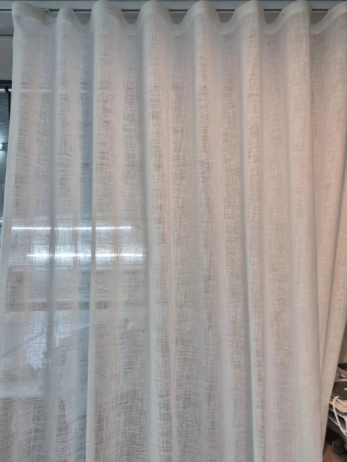 Close-up of gauzy white linen-look sheer draperies diffusing bright window light, showing the fabric's open weave texture