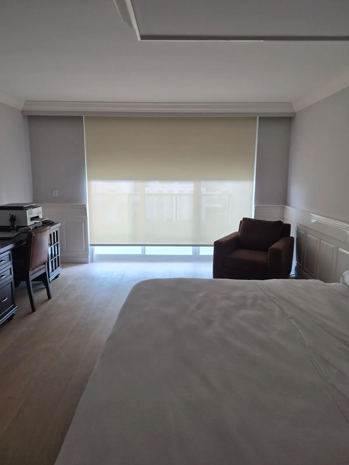 Grey blackout roller shade over a balcony sliding door, palm trees and a coastal street visible through the gap below