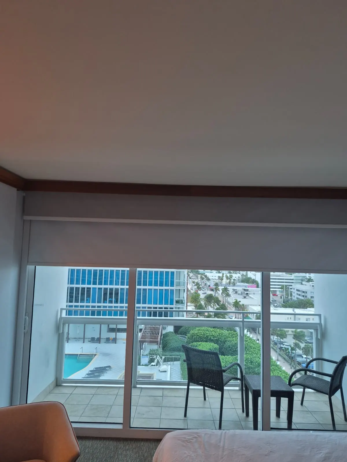 Cream blackout roller shade partially lowered over a balcony sliding door, palm trees and a pool deck visible below