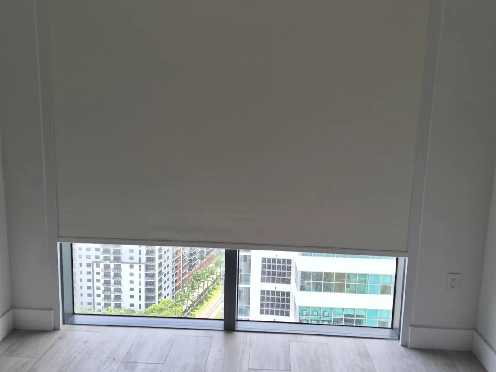 Cream roller shade with visible side channels tracking both edges of a high-rise sliding door