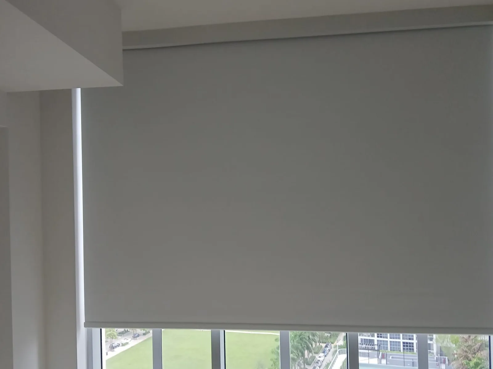 Grey roller shade with a visible side channel, overlooking a park and lawn below