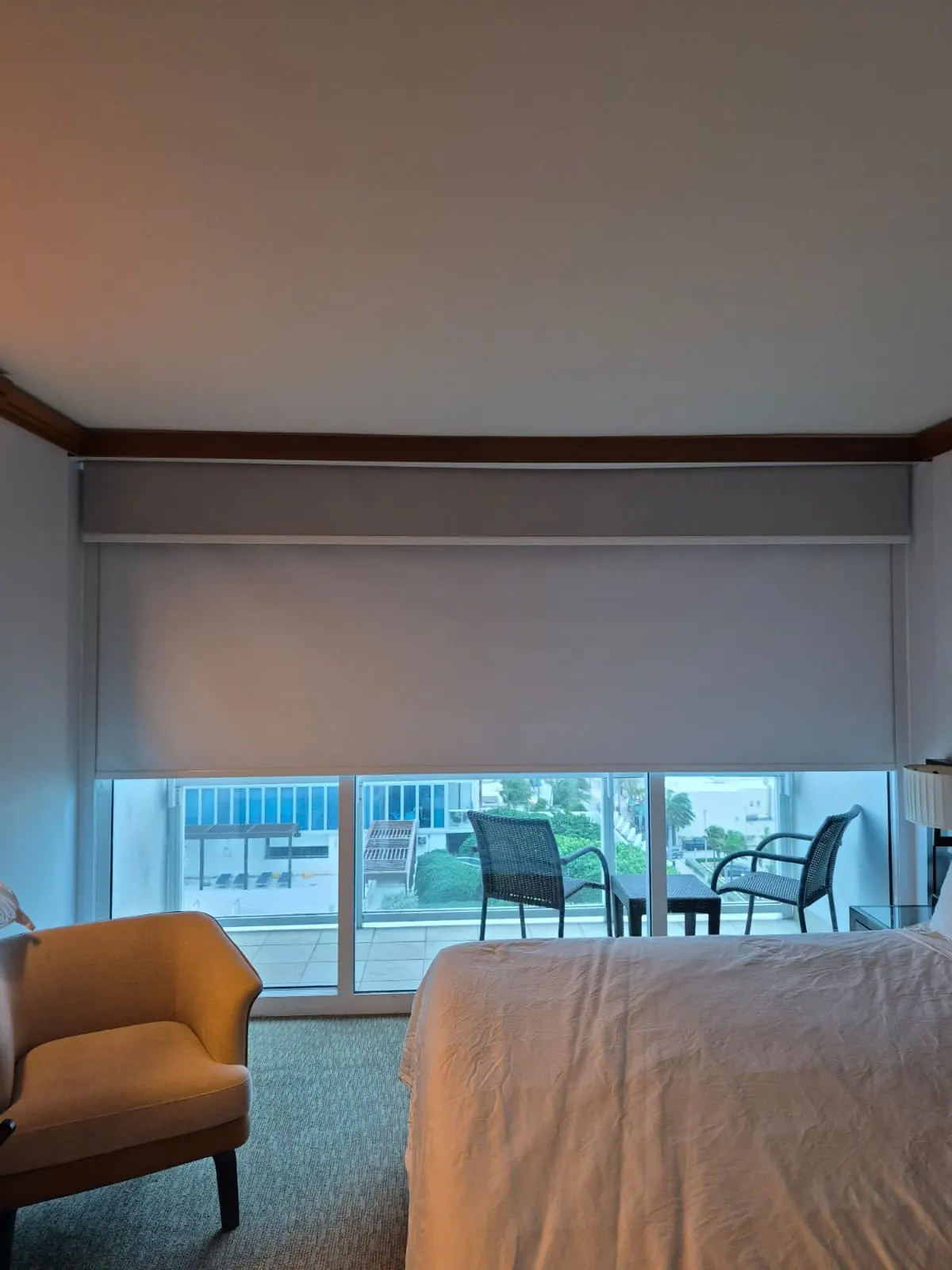Solar screen roller shades lowered over a corner window, translucent fabric revealing the Miami skyline and bay beyond