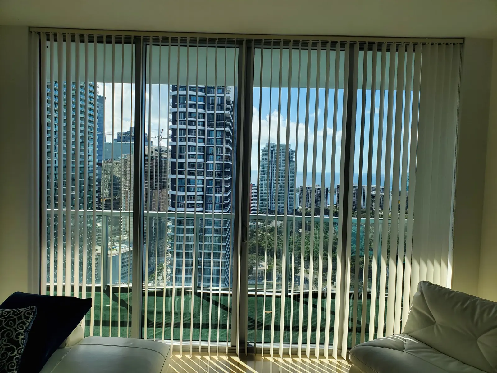 Ivory vertical blinds spanning a full wall of sliding glass doors, with a sunny bay and city skyline visible through the gaps