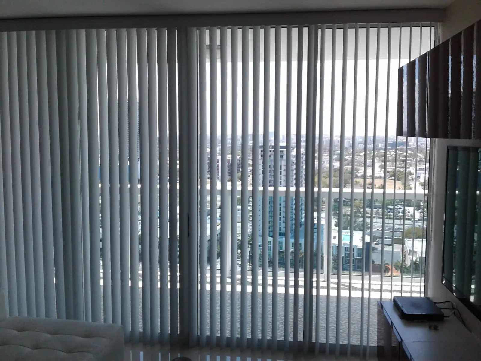 Blue-gray vertical blinds drawn across a sliding glass door, city skyline visible through the slats