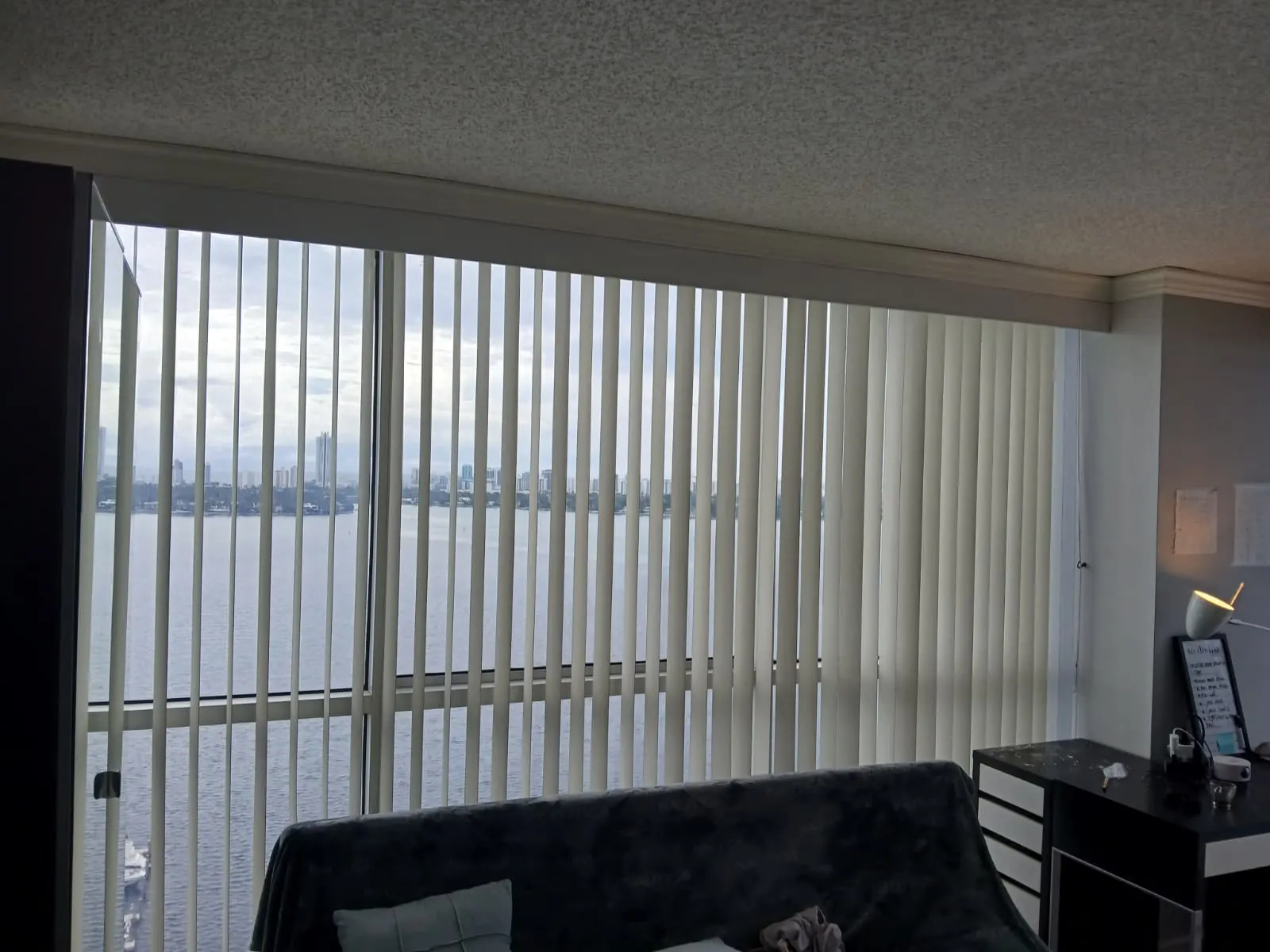 Cream vertical blinds partially drawn across a sliding door overlooking a bay and distant skyline
