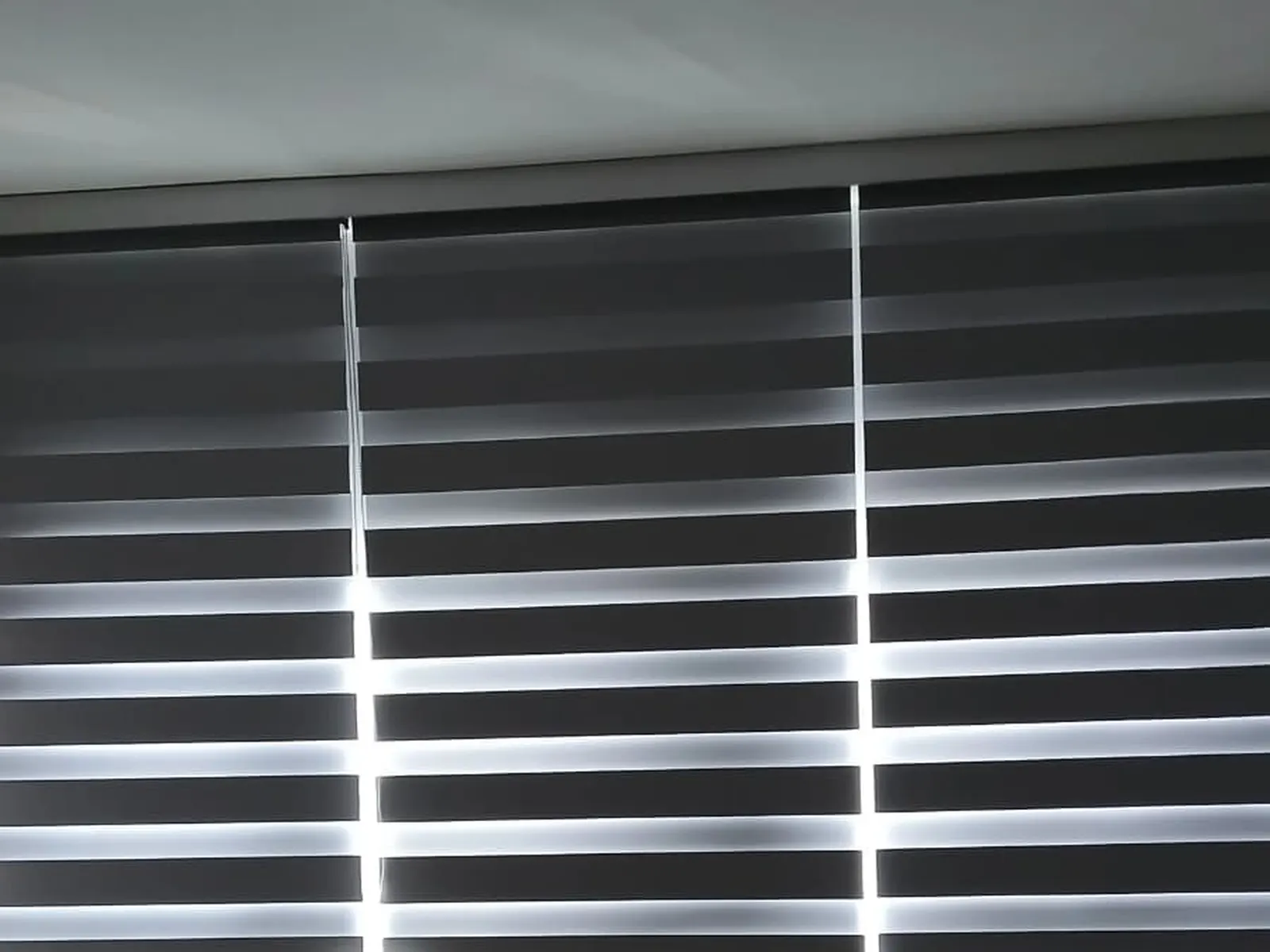 A three-panel zebra shade in charcoal and white stripes, close on the header rail and ceiling line of a second bedroom install