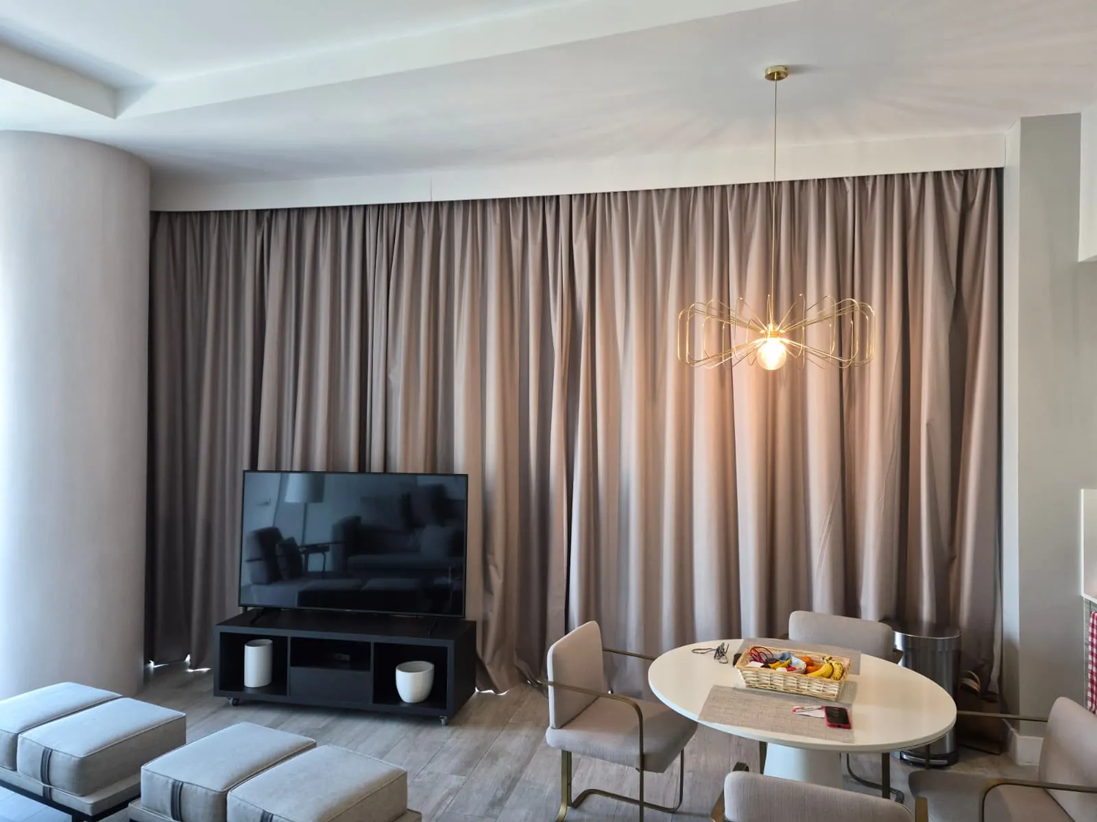 Two zebra shade panels across corner windows, cream sheer and solid bands filtering daylight, with a wall-mounted TV to the side